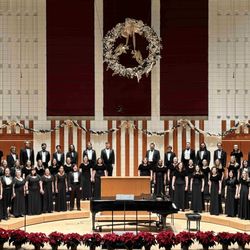 Choirs sings on a stage decorated with poinsettias and a large wreath